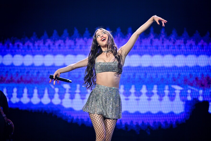 Pop artist Olivia Rodrigo dances on stage in front of a blue background.