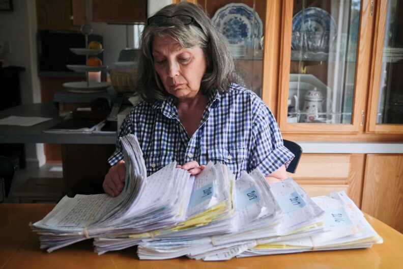 A gray-haired woman going through stacks of handwritten letters.