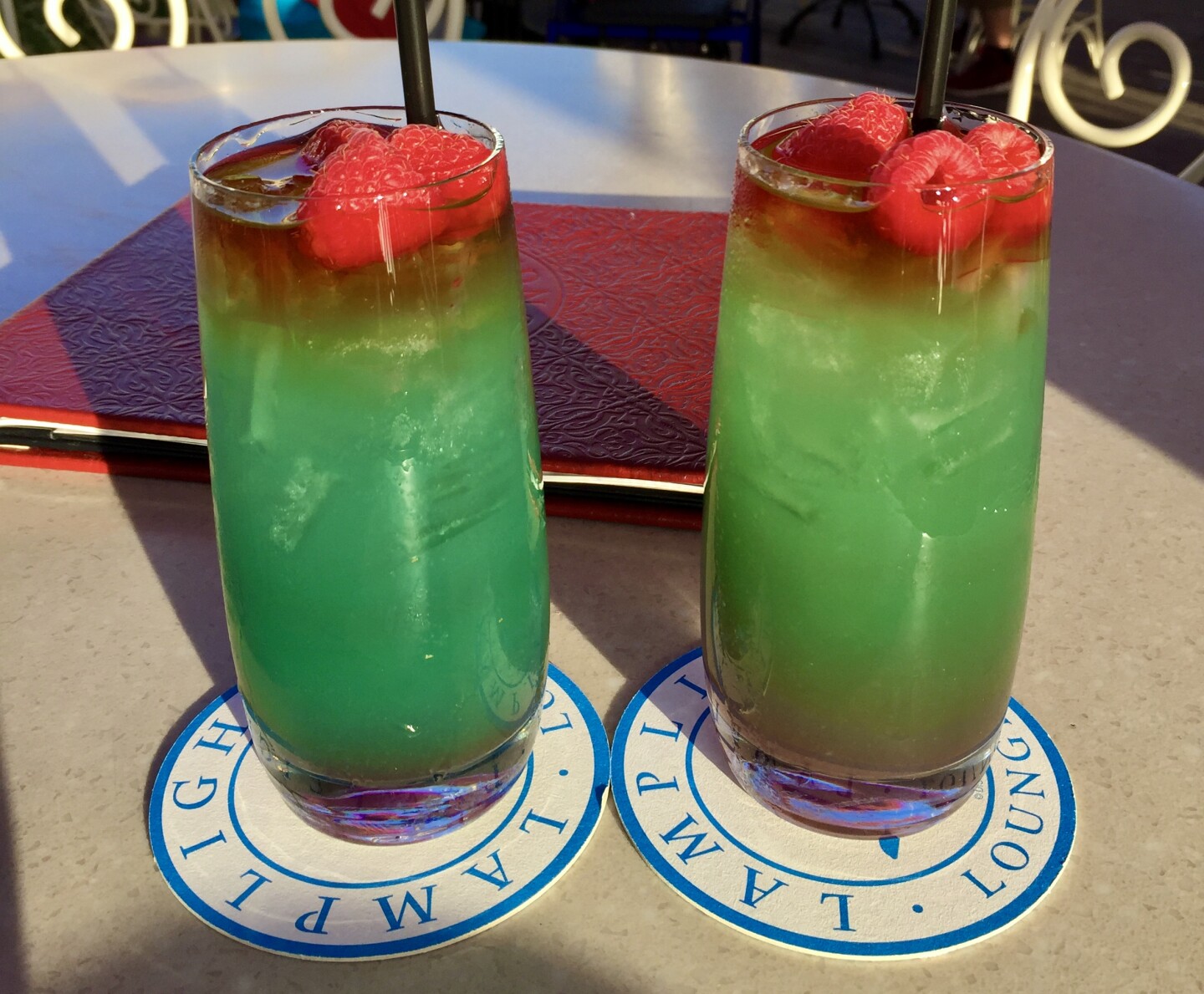 two tall glasses of green liquid topped with a few raspberries
