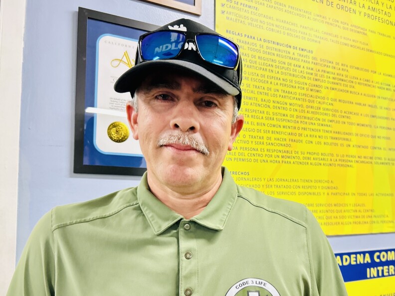 A male presenting person with a mustache, wearing a baseball cap.