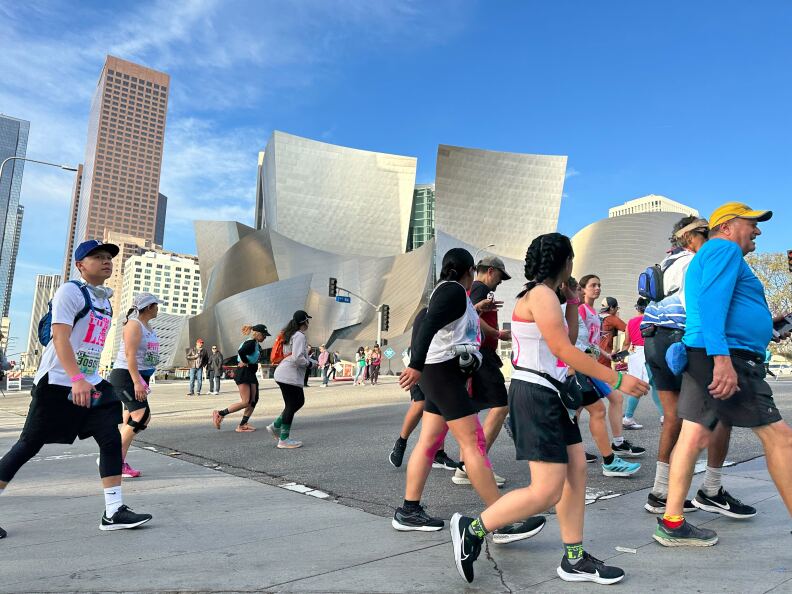 Runners and walkers running past a silver building in odd shape