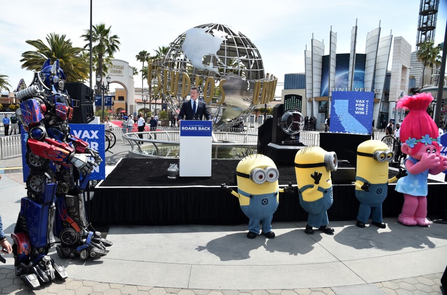 An image of Gov. Gavin Newsom's press conference at Universal Studios on June 15, 2021, the day the state's economy reopened. Newsom is joined by Los Angeles city leaders and residents, plus some costumed characters from the theme park.