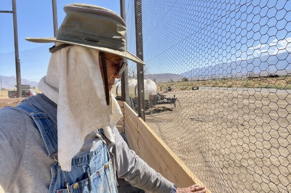 Person with hat and glasses faces wood and wire fence.