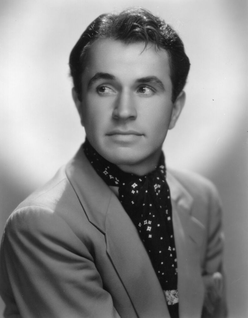 a black-and-white headshot of a man in a suit jacket and ascot