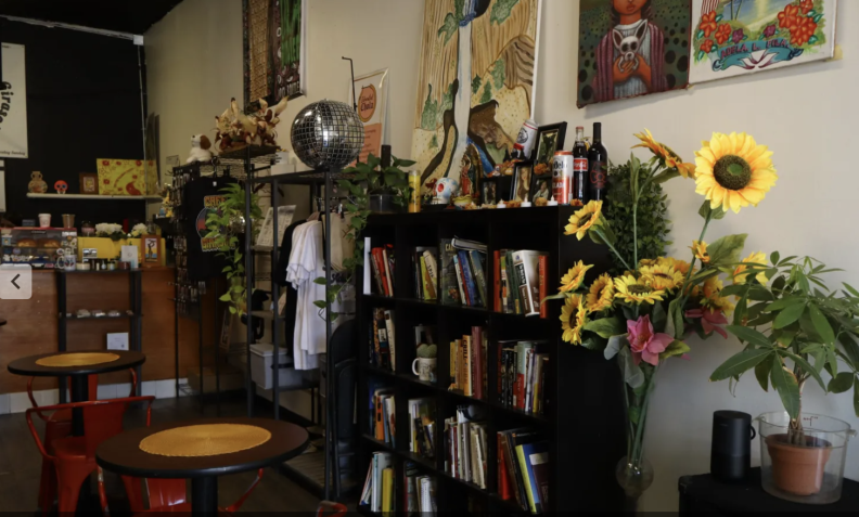 The interior of a coffee shop, with a colorful jumble of books, flowers, disco ball, clothes, and art on the wall