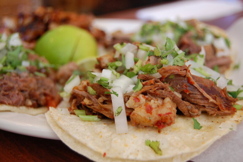 Four birria tacos on a plate with shredded onions on top