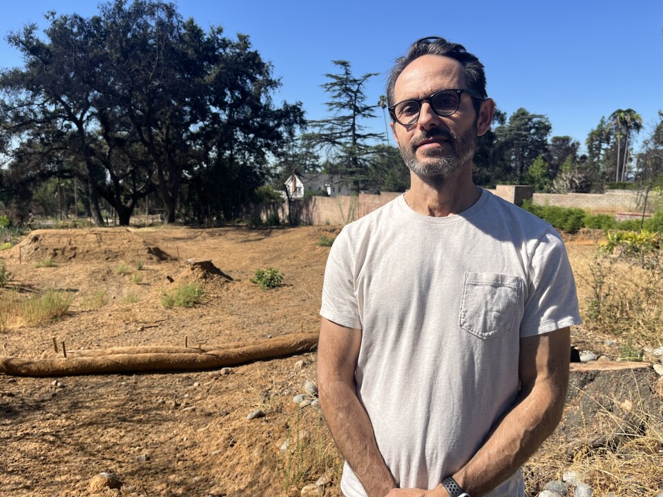 A man with medium-light skin tone stands on the dirt lot in Altadena where he plans to build smaller, more affordable homes made from fire-resistant materials. 