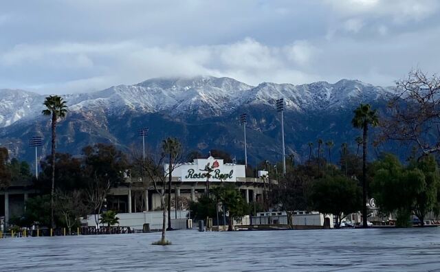 snow capped mountains rise above the Rose Bowl stadium with palm trees in the foreground