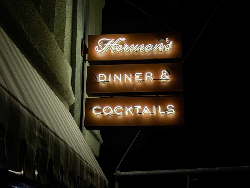 A nighttime view of Hermon’s neon sign reading “Dinner & Cocktails” glowing against the dark exterior.