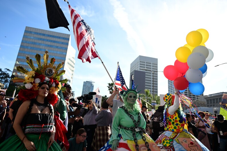 A crowd of people dressed in costumes stand together with some holding the American flag, signs and balloons.