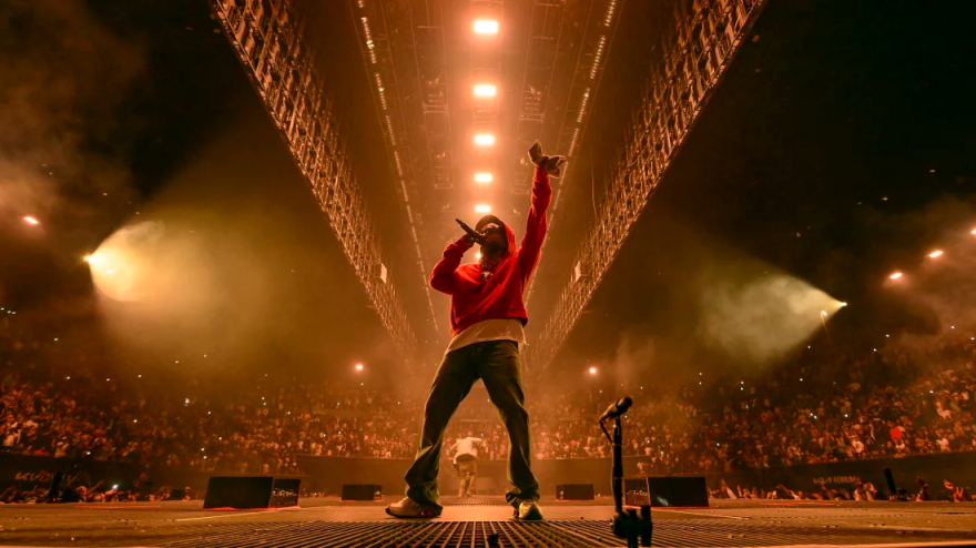 A man in a red sweatshirt stands on a stage with a mic in hand