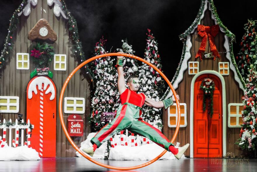 A performer wearing red and green rotates within a large hoop.
