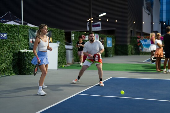 Image is two people on the same team playing waffle ball on a smaller sized tennis court.