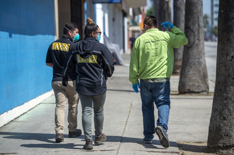 Two men and a woman walk down the street in Los Angeles while wearing masks to protect against COVID-19.