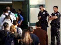 Los Angeles School Police officers watch students lining up to pass through a security check point on April 21, 2005, in the aftermath of two apparent racially motivated student brawls at Thomas Jefferson High School.