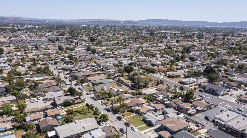 A aerial view of a city shows blocks of streets lined with pine trees and green lawns.
