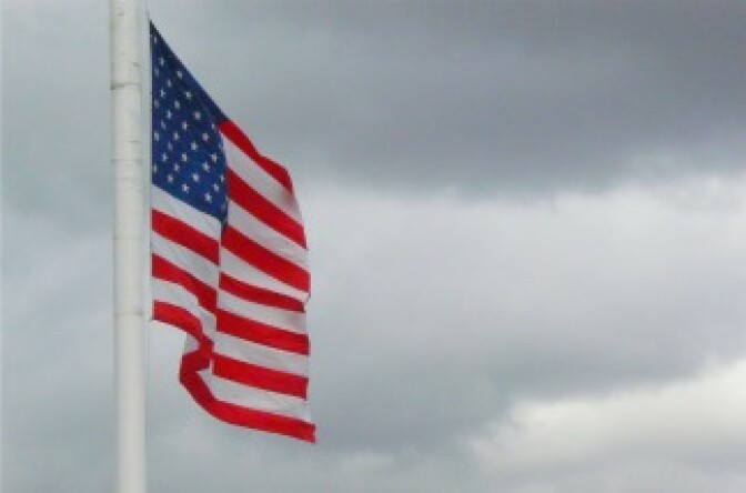 An American flag flies in a cloudy sky.