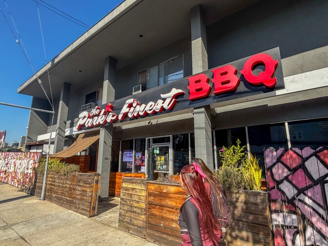 Street view of The Park’s Finest BBQ, a Filipino American barbecue restaurant with a black-and-red sign and outdoor patio on a sunny day.
