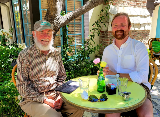 Donald Shoup and Nolan Gray sit around a lime green table with a green glass bottle in the middle holding pink and yellow flowers. 