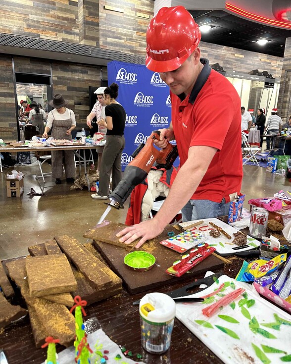 A man in red constructure hat using an electric handsaw to cut a gingerbread