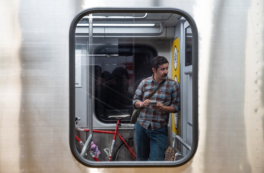 A man stands in a subway car next to a red bicycle.