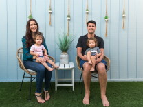 Two parents holding their children in chairs by a plant