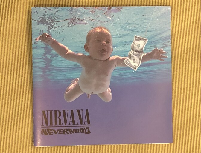 A naked baby underwater in a pool swims near a $1 bill.