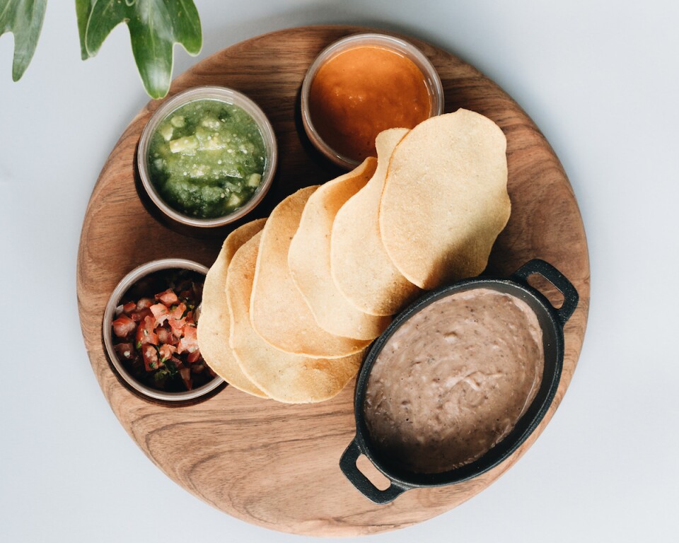 torillas on a circular serving tray surrounded by dishes of refried beans and salsas