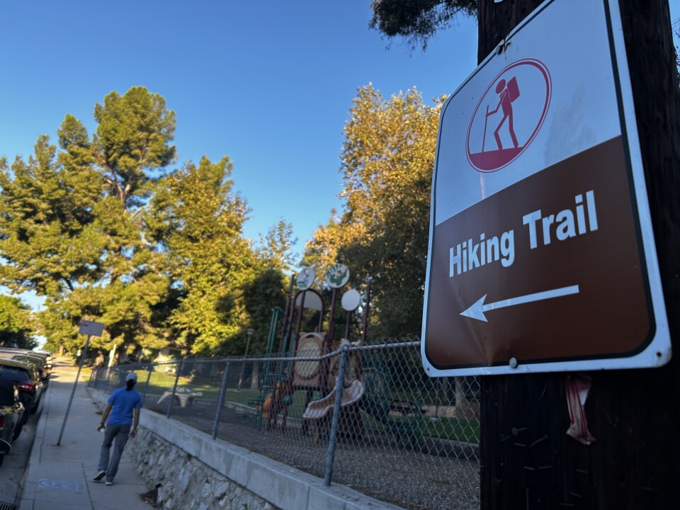 A wide image of a rectangular metal sign that says "hiking trail" on a electrical pole with an arrow pointing left