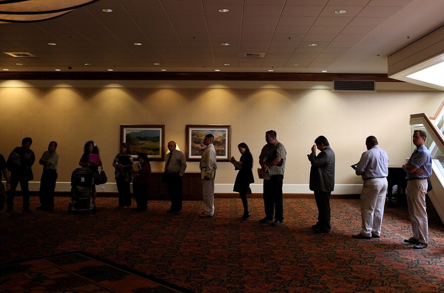 Job seekers read pamphlets as they wait in line to enter a job fair.
