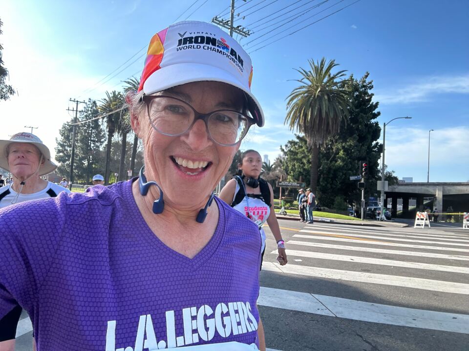 A woman in glasses and a purple running shirt smiling big into the camera.