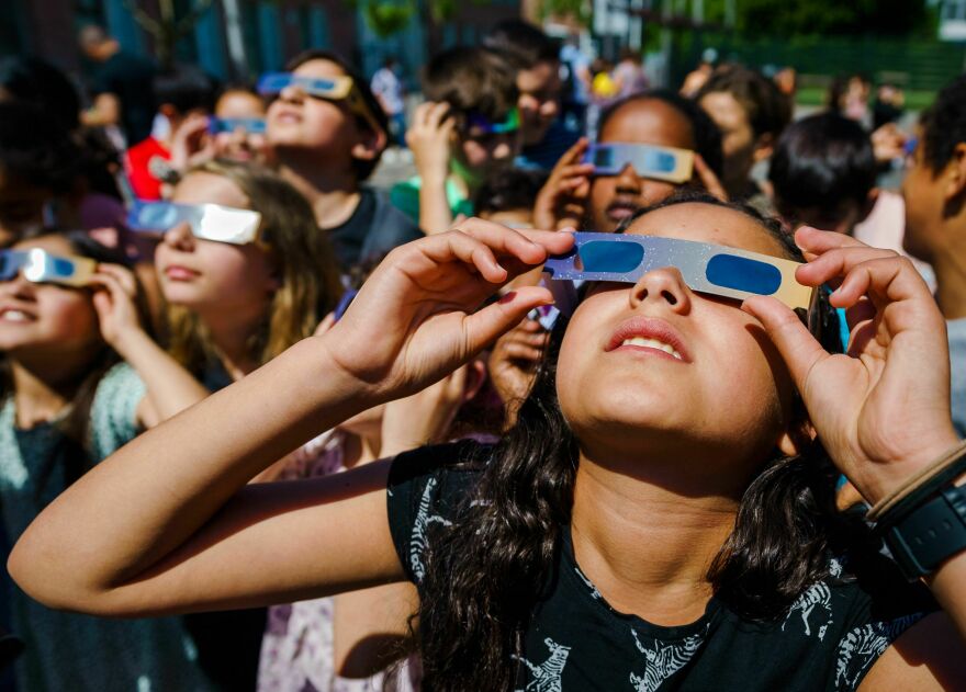 A group of people binoculars and special glasses to look up at the sky.