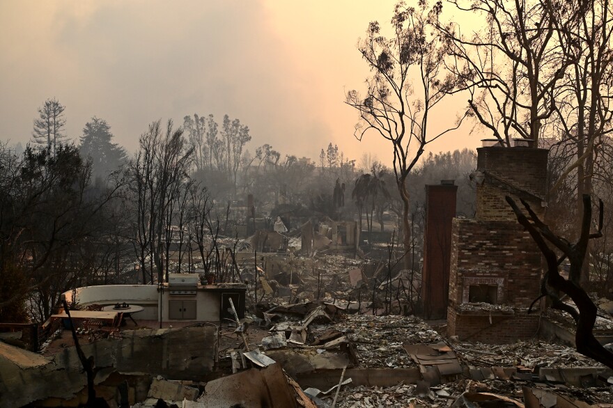 Properties flattened by fire, smoke billows in the air.