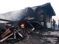 A burnt house, with fire still burning on the ground. 