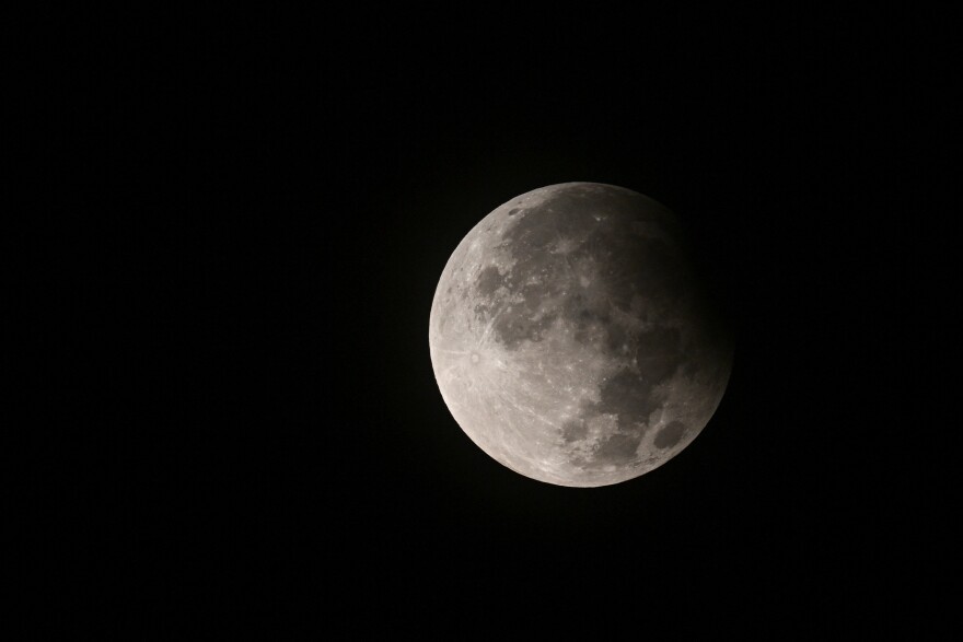A stunning white moon with craters is outlined against a dark blue sky