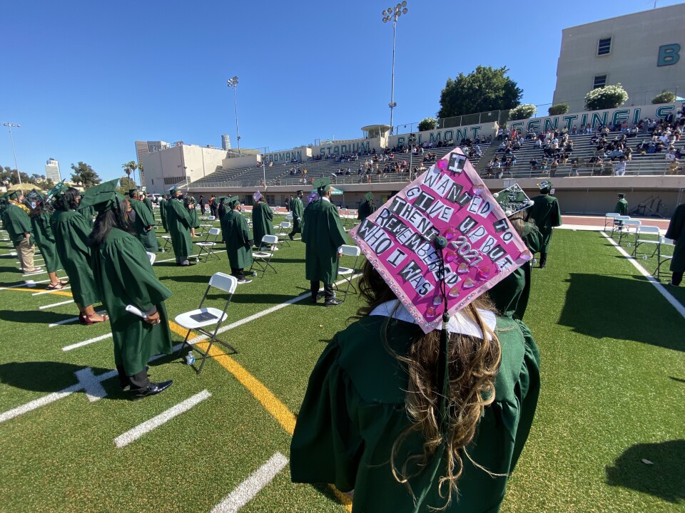 During the commencement ceremony at Belmont High School, an L.A. Unified School District campus near downtown, a graduating senior wears green robes and a mortarboard decorated with the words: "I wanted to give up but then I remembered who I was." She's standing on a football field next to other graduating students who are assembled at socially-distanced folding chairs.