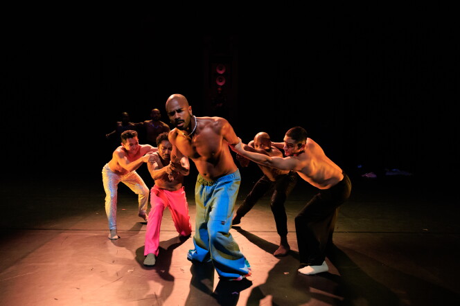 A group of people in the middle of a dance performance. One person, centered, is being held by the arms by four others surrounding them.