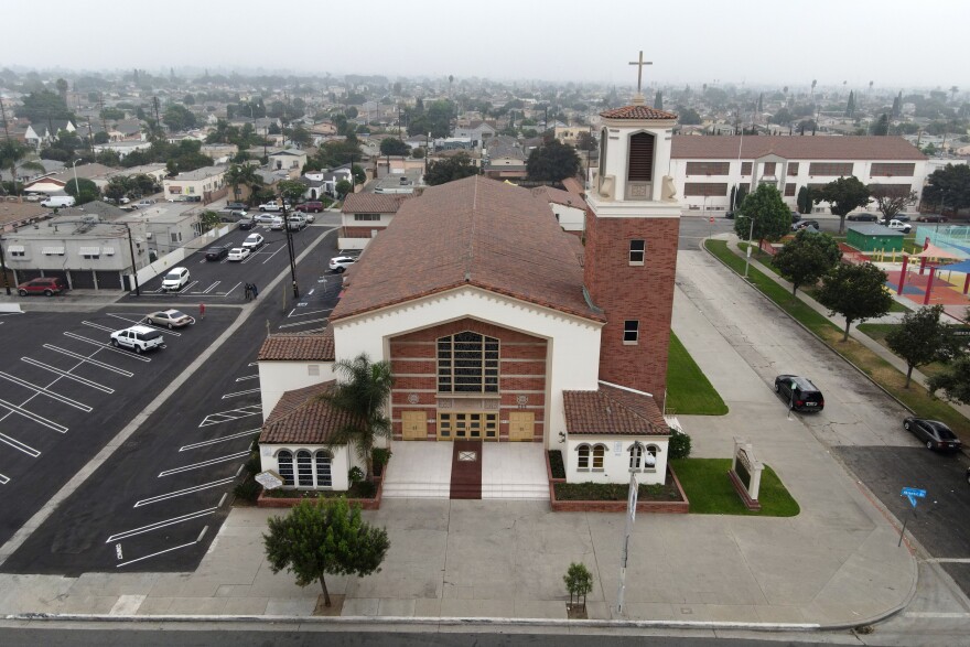 A large church as seen from above features a Spanish tile rook and a red bring spire with a cross on top.