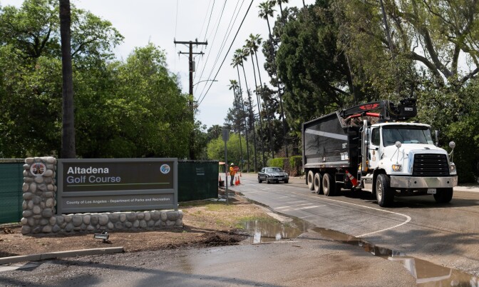 A truck on the street with a car behind it and a sign to the left reading "Altadena Golf Course."