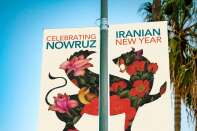 A banner on a streetlight reads "Celebrating Nowruz, Iranian New Year" at UCLA on March 9. It features a winged lion-griffin adorned with nightingales and flowers. In the background, the tops of palms trees can be seen. 
