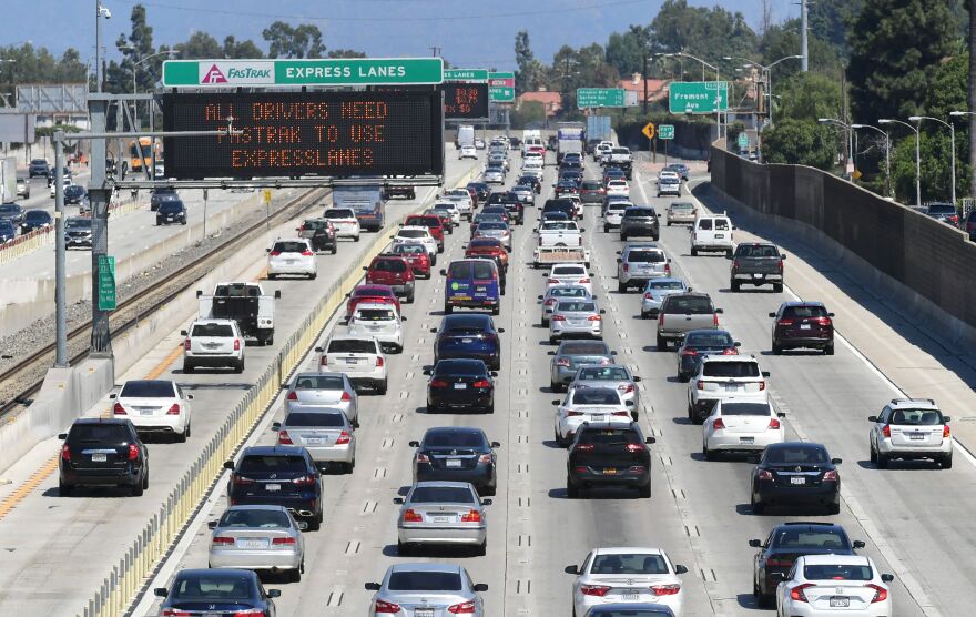 Cars are backed up on a freeway with five lanes of traffic, with a separate express lane towards the middle. It's a sunny, clear day.