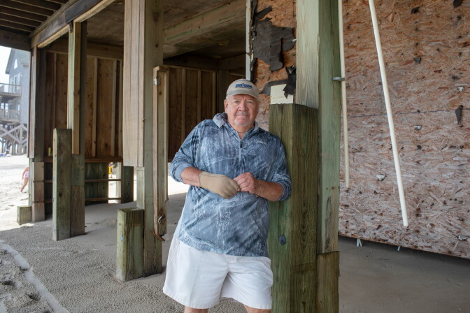 A white man standing in front of a house that's falling apart.