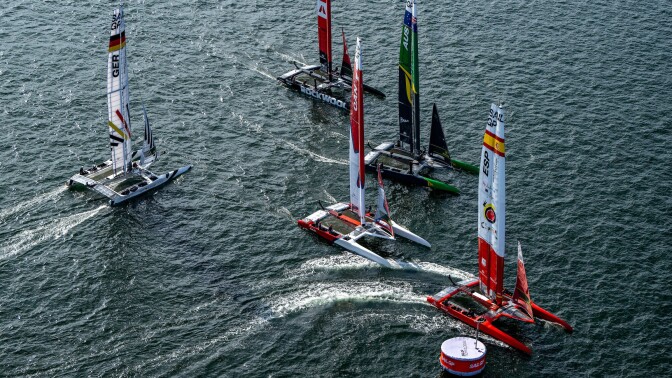Five catamarans sailing in open water during a race. They're varying colors to represent different countries, including Spain, Canada, Australia and Germany. 