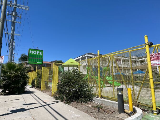  A yellow fence surrounds a 3-story motel building and a playground. A green sign labeled "Hope" sits in front of the property. 