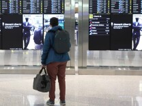 a person with a backpack and a bag looks at a board of flight information