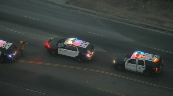 A still from an image shot by NBC4 shows a suspect (in middle car, stolen) fleeing a squad car as an L.A. Sheriff's Department deputy points his gun at the suspect.