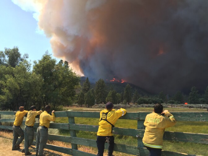 Firefighters watch from the Lake Hemet Campground near the incident command post for the Cranston Fire as flames crawl over Baldy Mountain.