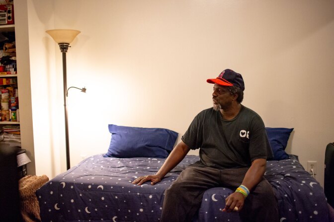 A man sits on a bed looking off to the left.