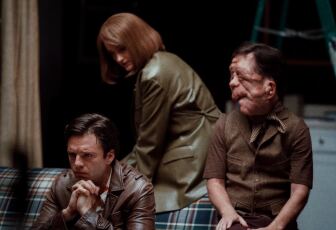 Two men sit on a couch. A woman leans in behind them.