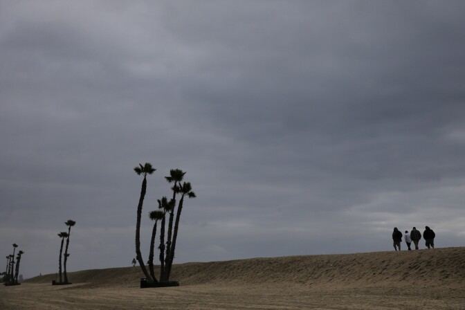 People walk along the sand wall Thursday, Dec. 11, 2014, in Seal Beach, Calif. High winds and heavy rains caused flooding and landslides in the Pacific Northwest on Wednesday, and the southward-moving storm was expected to pound parts of Southern California Thursday evening. (AP Photo/Jae C. Hong)
